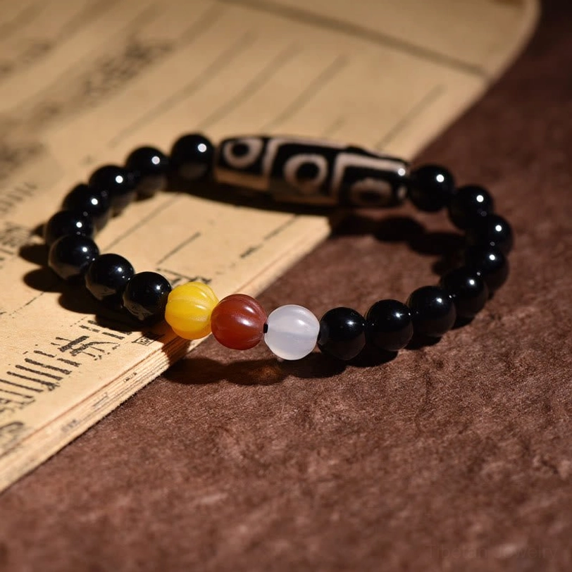 Tibetan nine-eye dzi bead bracelet detail shot on antique scroll, showing yellow-red-white spacer bead arrangement and classic nine-eye etched agate design