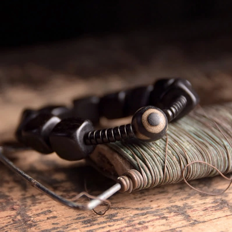 Sacred nine-eye dzi bead bracelet with smooth black square ebony beads spiral spacers and protective dzi on wooden surface
