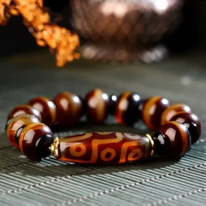 Nine-eye dzi agate bracelet flat lay on bamboo mat with natural dried flowers and striped brown agate beads with gold spacers