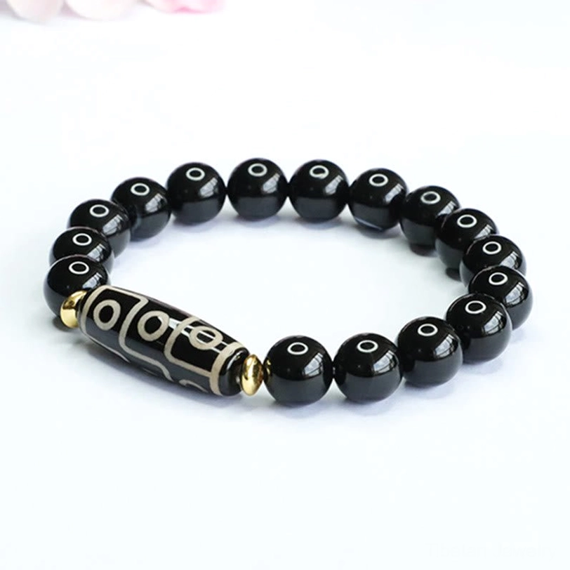 Flat lay top-down view of nine-eye dzi bead bracelet featuring centered dzi bead with black onyx beads and gold spacers