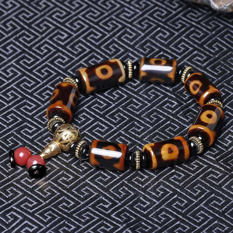 Nine-eye dzi bracelet flat lay on geometric textile background showing loop-style design with gold guru bead and red accent bead