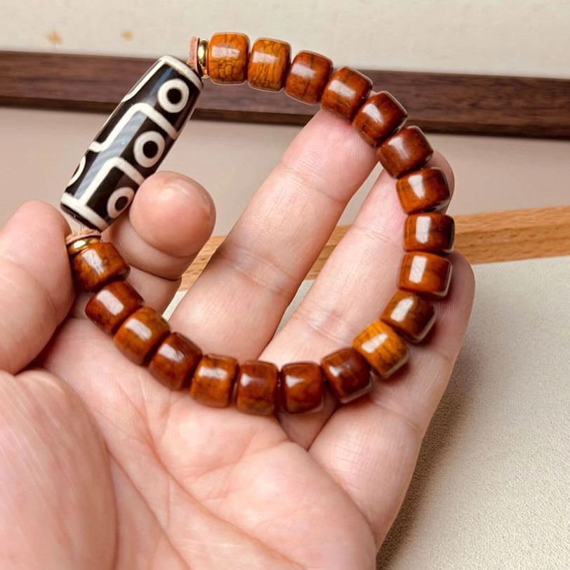 Close-up view of nine-eye Dzi bone bracelet held in human palm showing detailed bead design