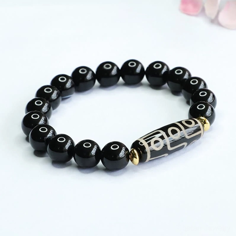 Top-front overhead view of nine-eye dzi bead black onyx bracelet with polished beads and long patterned dzi bead on floral backdrop