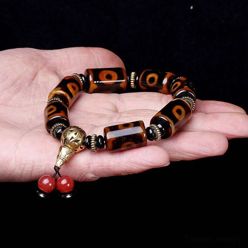 Nine-eye dzi bead bracelet worn on human palm against dark background, showcasing classic dzi eye patterns and natural agate texture in hand