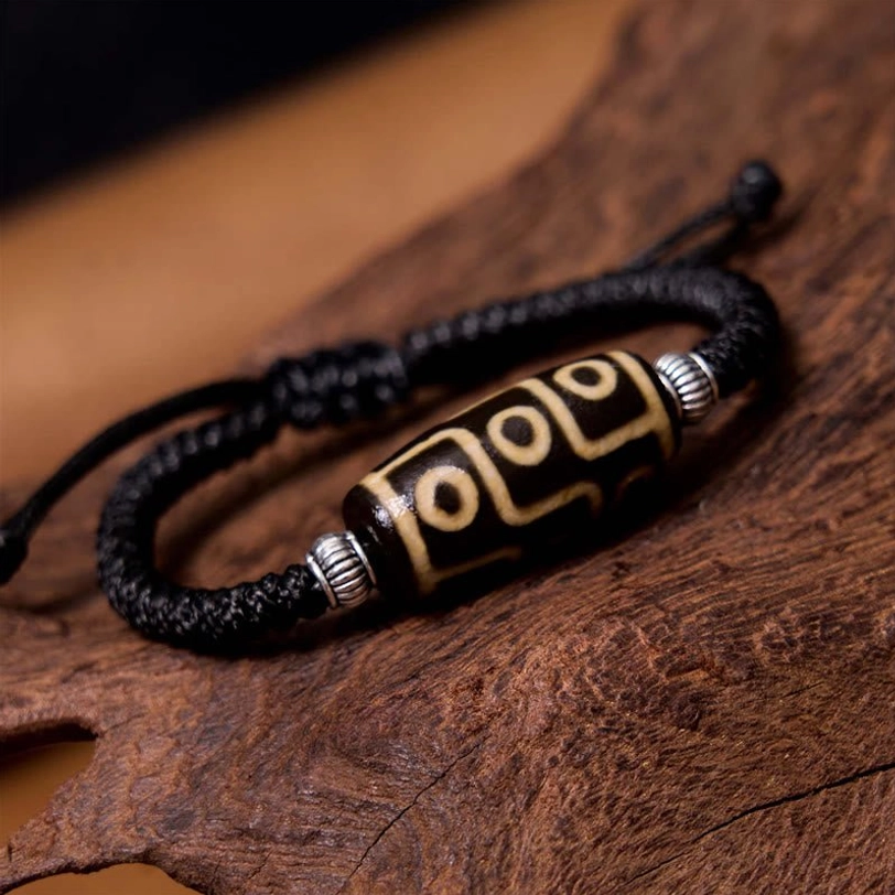 Nine-eye dzi bead bracelet oblique side view showing braided black cord with silver accents and traditional nine-eye pattern detail