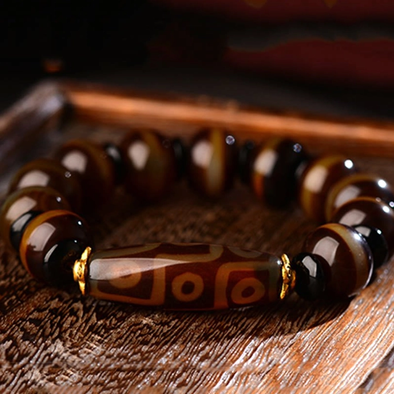 Nine-eye dzi agate bracelet overhead flat lay on wooden table showing glossy brown striped agate beads with gold metal accents