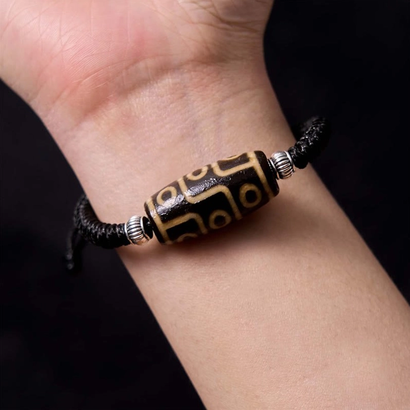 Dzi bead bracelet worn on wrist close-up side view showing black woven rope and nine-eye bead placement