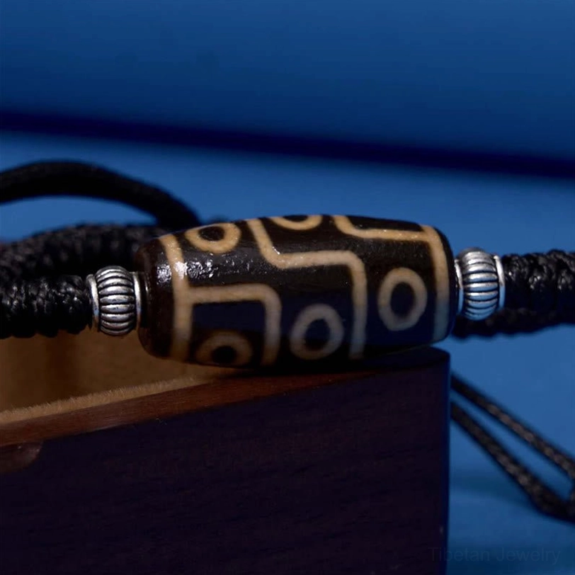 Macro close-up of nine-eye dzi bead pattern showing intricate hand-painted details with black rope and silver metal accents