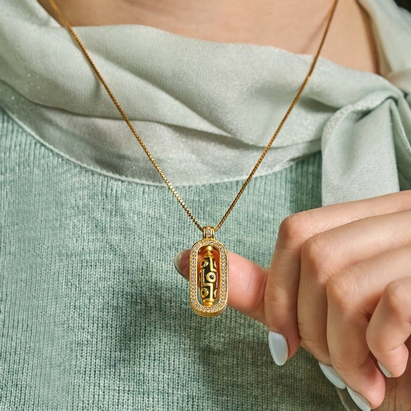 Nine-eye dzi bead necklace worn on person with light green top, first-person styling view, thin gold chain