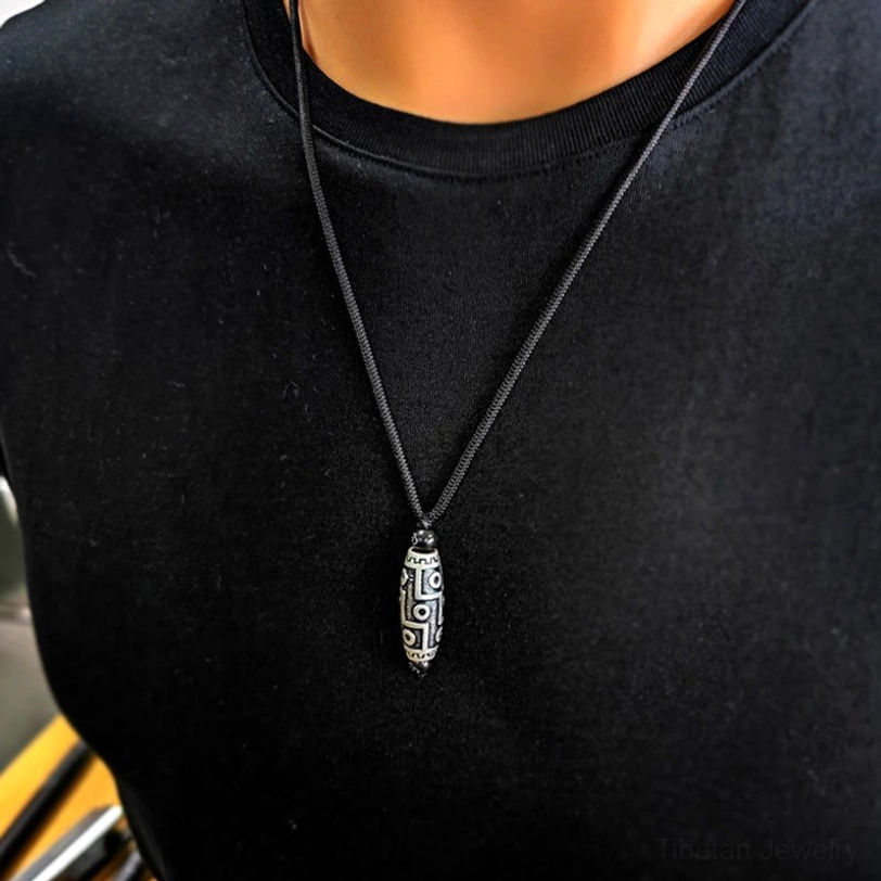 Nine-eye dzi pendant necklace worn on black crewneck demonstrating slim elegant silhouette and everyday wearability