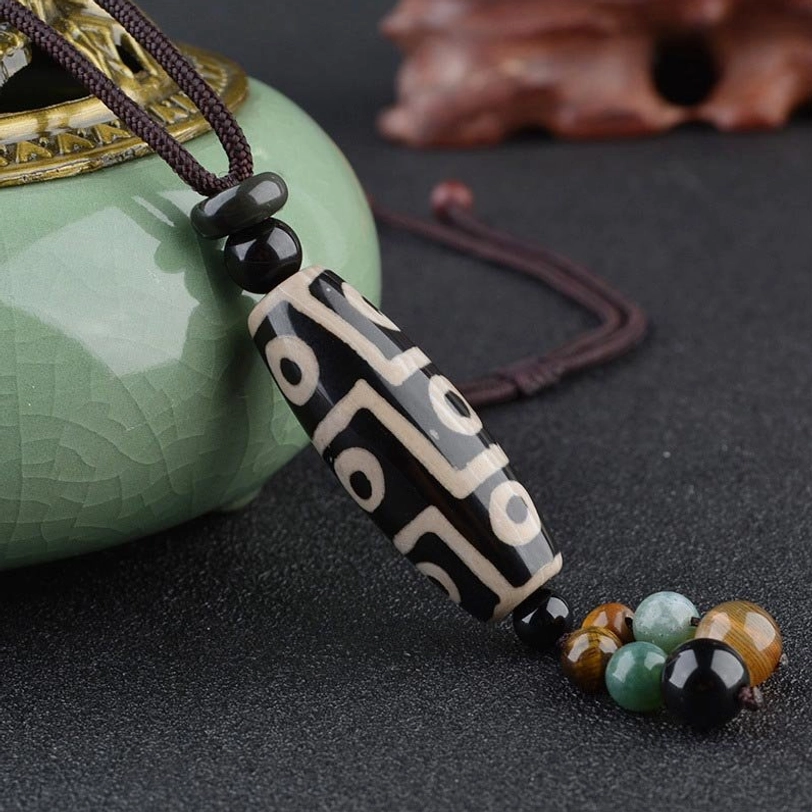 Nine-eye Dzi bead pendant necklace with black and white agate pattern, jade tassel details, and hand-woven cord on porcelain display