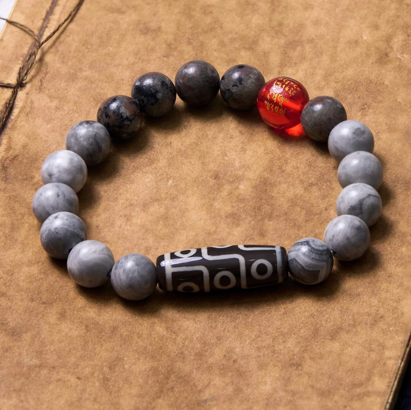 Handmade nine-eye dzi jasper bracelet flat lay on vintage brown paper, showing darker matte grey beads and protective dzi amulet design