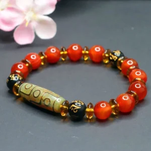 Nine-eye dzi bead red agate bracelet displayed at oblique angle with pink cherry blossom decoration, showing amber and gold-tone metal spacer beads
