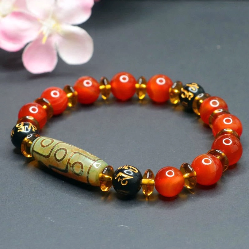 Nine-eye dzi bead red agate bracelet displayed at oblique angle with pink cherry blossom decoration, showing amber and gold-tone metal spacer beads