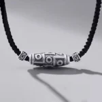 999 Sterling Silver Nine-Eye Dzi Bead Necklace with black braided rope cord, front overhead view showing detailed hand-engraved pattern