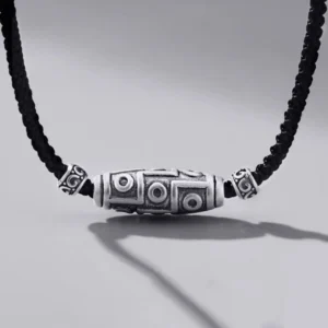 999 Sterling Silver Nine-Eye Dzi Bead Necklace with black braided rope cord, front overhead view showing detailed hand-engraved pattern