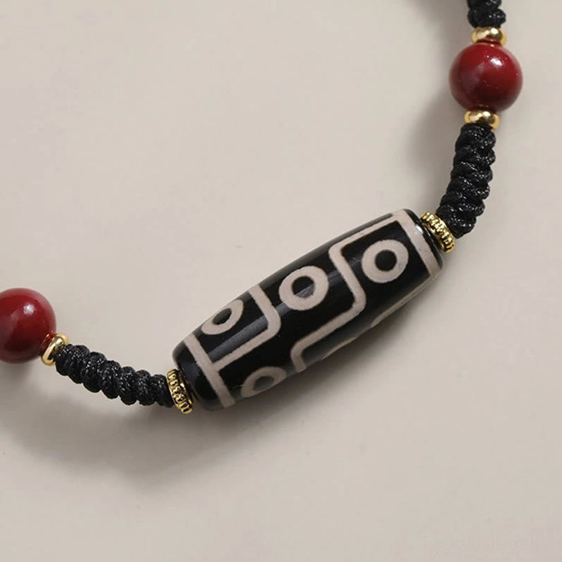 Nine-eye dzi bead bracelet close-up flat lay featuring red cinnabar bead and detailed eye pattern on dzi stone