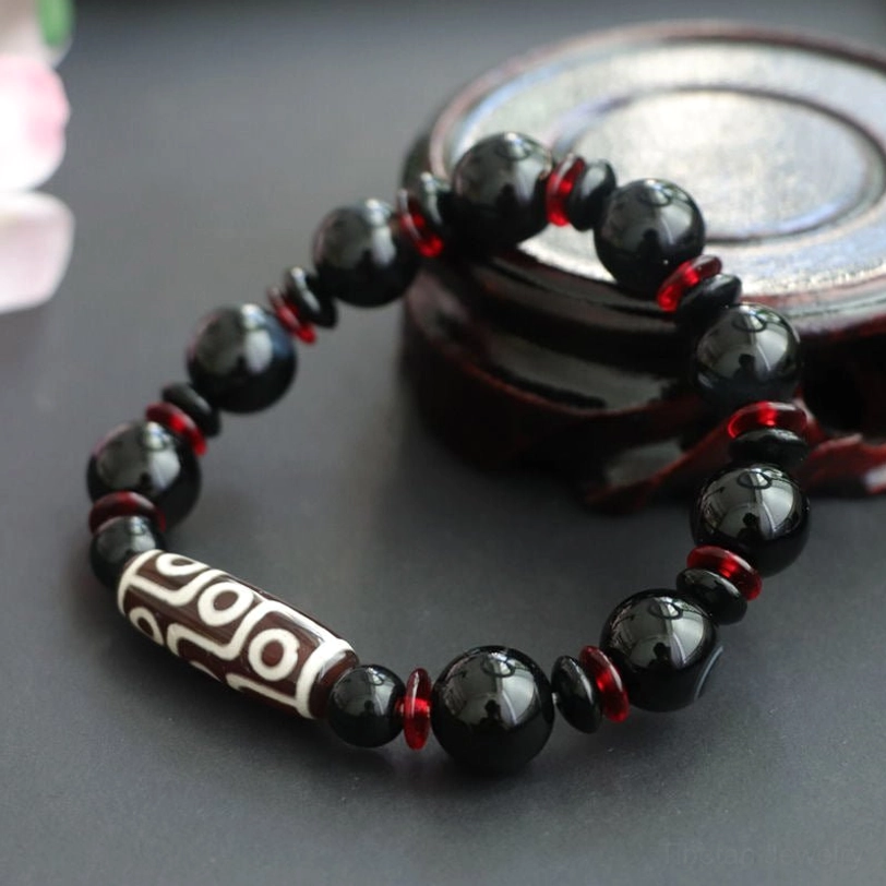 Black Onyx Nine-Eye Dzi Bead bracelet shown at angle with natural stone background, illustrating authentic hand-painted Dzi bead craftsmanship