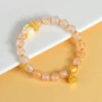 Nine-tailed fox lotus charm bracelet with tibetan incense ash glass beads in pink, displayed on white paper with gold metal accents and crystal spacers