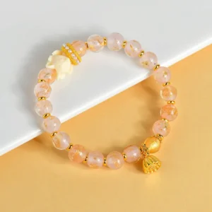 Nine-tailed fox lotus charm bracelet with tibetan incense ash glass beads in pink, displayed on white paper with gold metal accents and crystal spacers