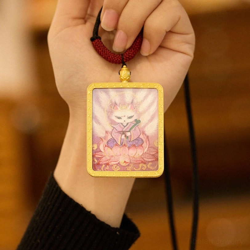 Close-up handheld view of Nine-Tailed Fox thangka pendant necklace with gold frame, showing pink fox-lotus artwork and red cord