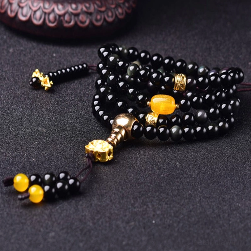 Tibetan 108 bead obsidian mala prayer beads with yellow barrel spacer and tassel counter detail on dark background