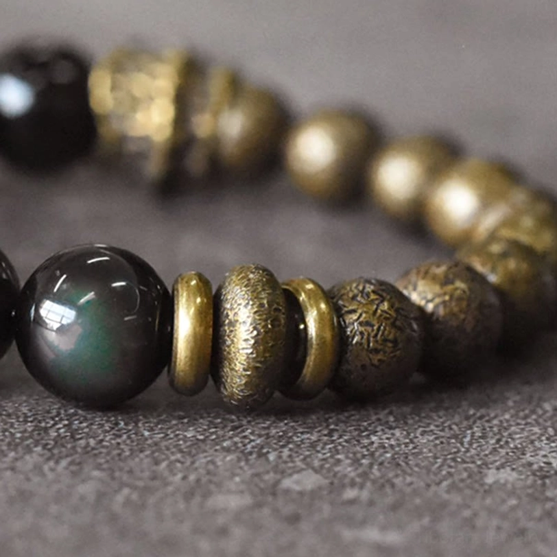 Beaded Bracelet Close-up Side View - Visible Rainbow Iridescent Sheen on Obsidian Bead with Engraved Bronze Metal Spacers