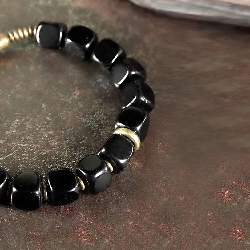 Black obsidian bracelet top-down side view on gray background showing hammered brass section and metal rings detail