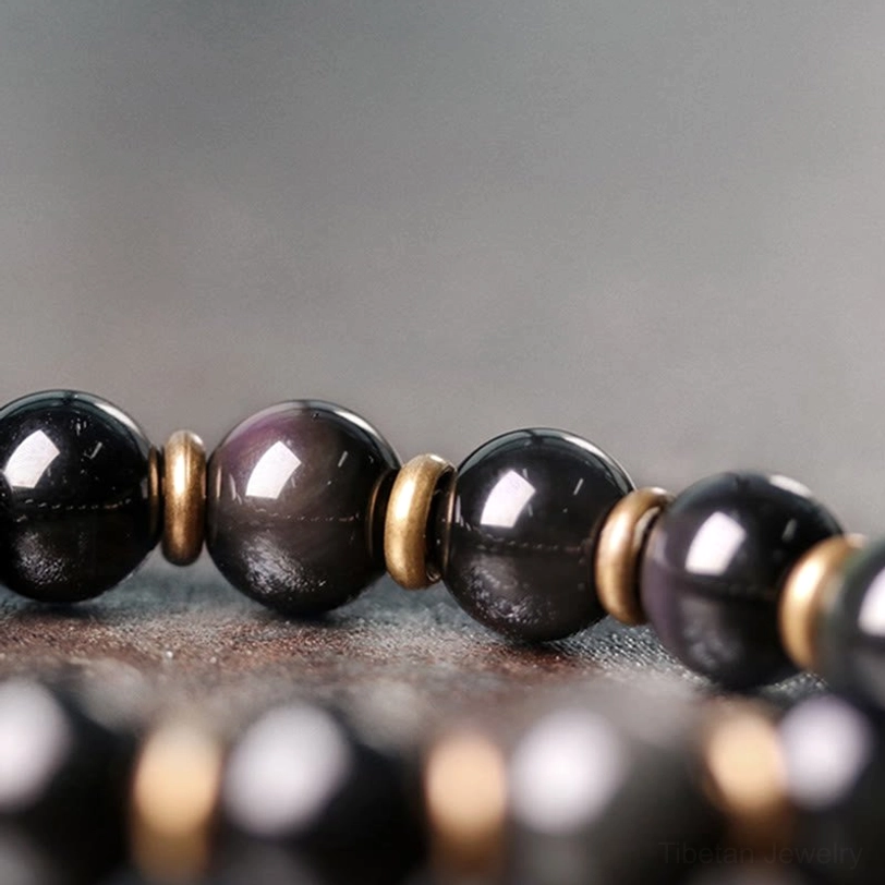 Obsidian bracelet beads and bronze spacer rings flat lay macro photography showing glossy surface