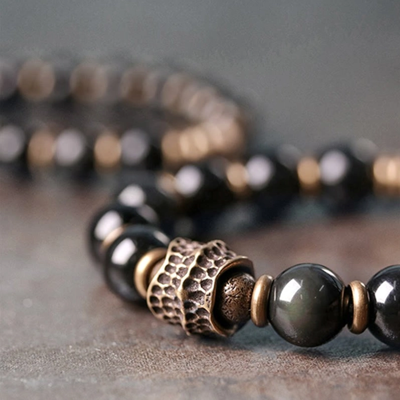 Rainbow obsidian bracelet side angle showing glossy black stone beads and metal charm details