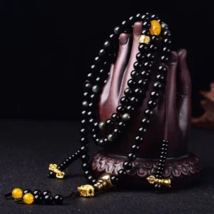 Black obsidian prayer beads mala displayed on wooden Buddha hand stand, showing polished beads and lotus tassel pendant detail
