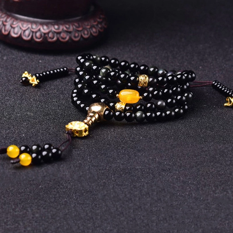 Black obsidian mala bracelet flat lay showing round polished beads, gold decorative components, and lotus flower tassel accent