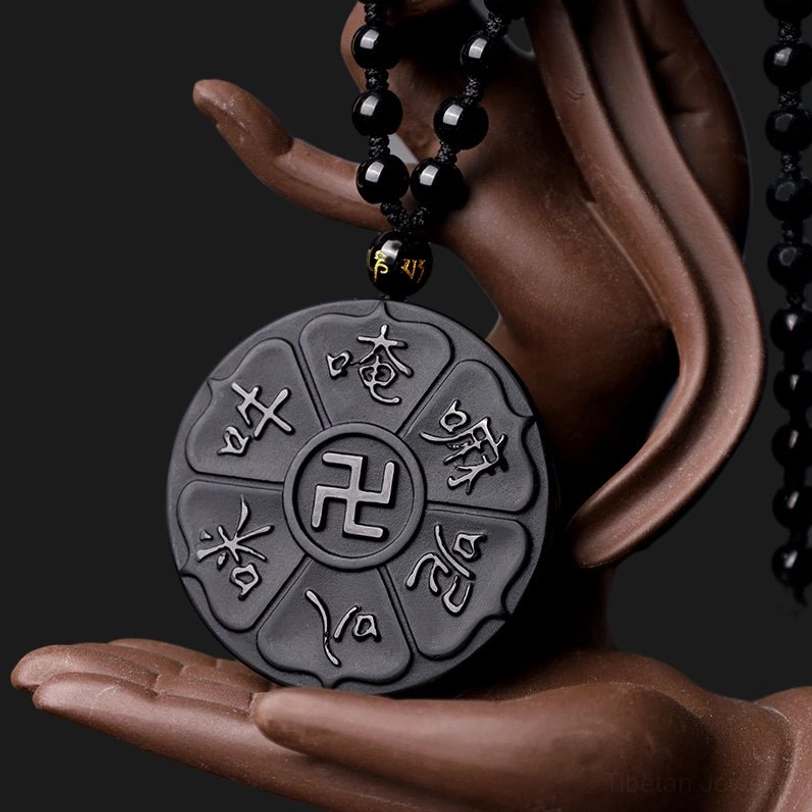 Sacred six-word mantra Om Mani Padme Hum engraved black obsidian pendant held in Buddha statue hand, close-up detail shot