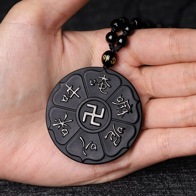 Matte black obsidian Tibetan Buddhist pendant in human palm, eye-level view showing swastika and six-syllable mantra engravings