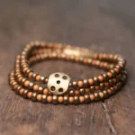 Handmade olive pit copper wealth bracelet with brass accents displayed overhead on wooden surface, showing warm brown beads and traditional four-hole brass clasp detail