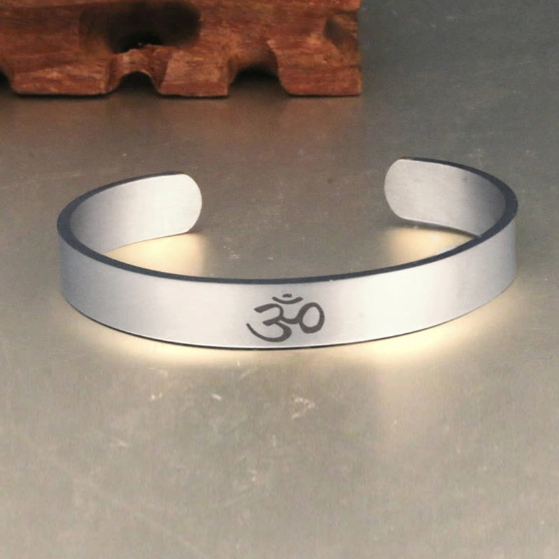 Front view of Tibetan OM open cuff bracelet showing adjustable design and engraved symbol on wooden tabletop