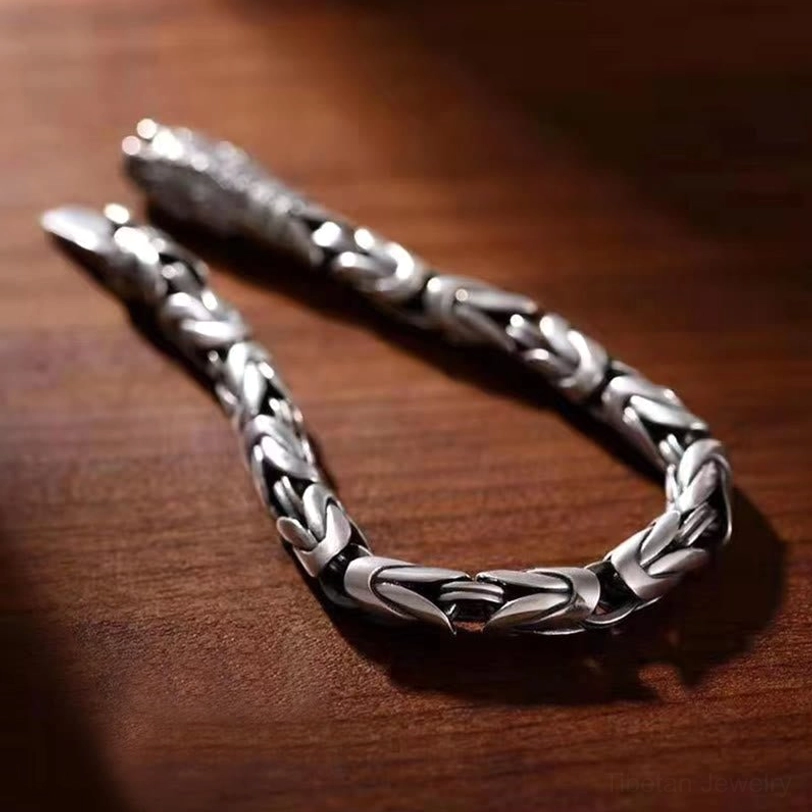 Close-up view of interwoven Om Mani Padme Hum copper bracelet showing braided chain structure and polished silver tone on wooden surface