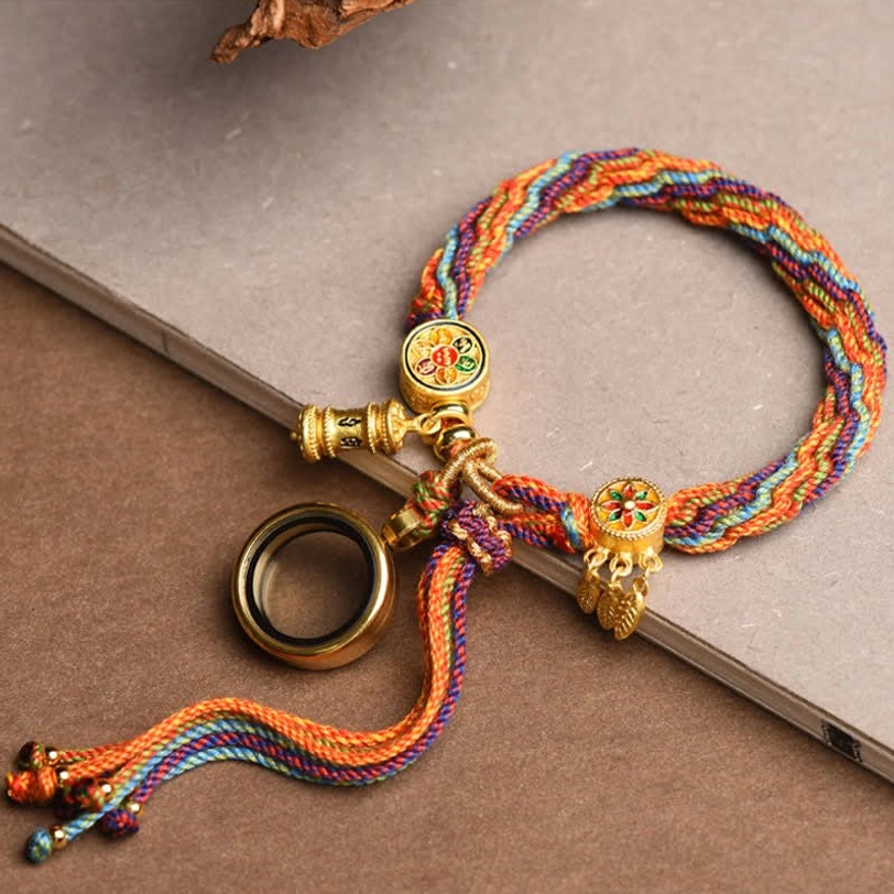 Tibetan dreamcatcher bracelet with rainbow braided rope and gold enamel charms on hardcover book display