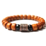 Tibetan Om Mani Padme Hum bone bead bracelet with carved metal charm and black spacer beads on white background