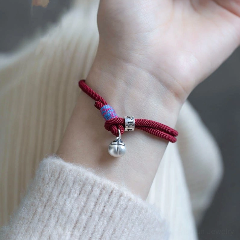 Wearing demo of red om mani padme hum persimmon charm bracelet on wrist with sweater background