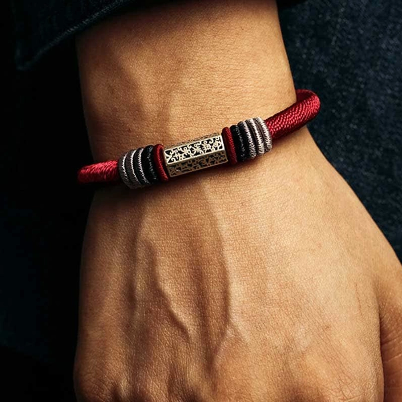 Close-up side view of Om Mani Padme Hum red cord bracelet on wrist showing engraved silver charm detail