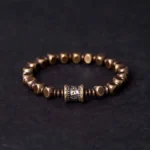 Om Mani Padme Hum brass meditation bracelet with engraved mantra bead, front view on dark background