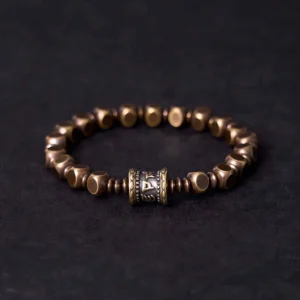 Om Mani Padme Hum brass meditation bracelet with engraved mantra bead, front view on dark background
