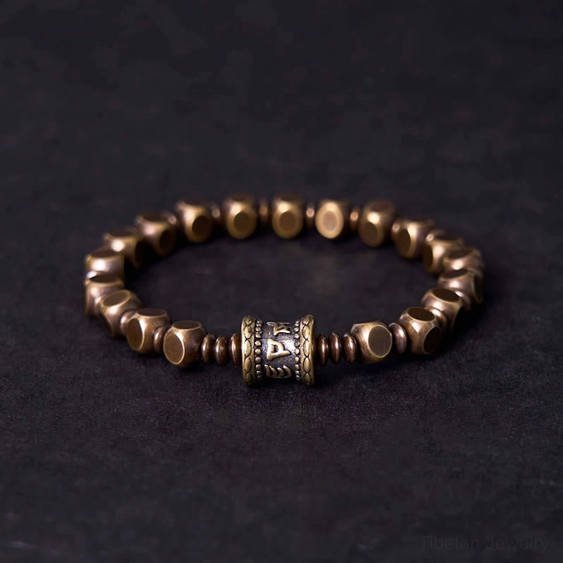 Om Mani Padme Hum brass meditation bracelet with engraved mantra bead, front view on dark background
