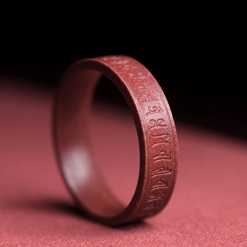 Om mani padme hum mantra carved cinnabar blessing ring close-up showing sacred six-syllable engraving and polished finish
