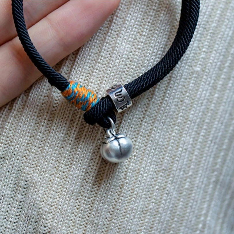 Close-up macro view of om mani padme hum persimmon charm bracelet showing silver bell and engraved bead