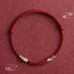 Om Mani Padme Hum red string blessing bracelet with cinnabar bead and sterling silver accents, flat lay overhead view