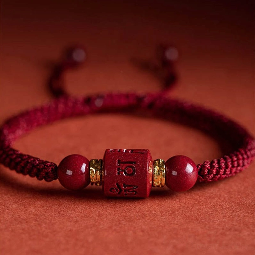 Close-up detail of Tibetan Om Mani Padme Hum cinnabar bracelet showing engraved Sanskrit mantra bead, round cinnabar beads, gold metal spacers, and woven red rope