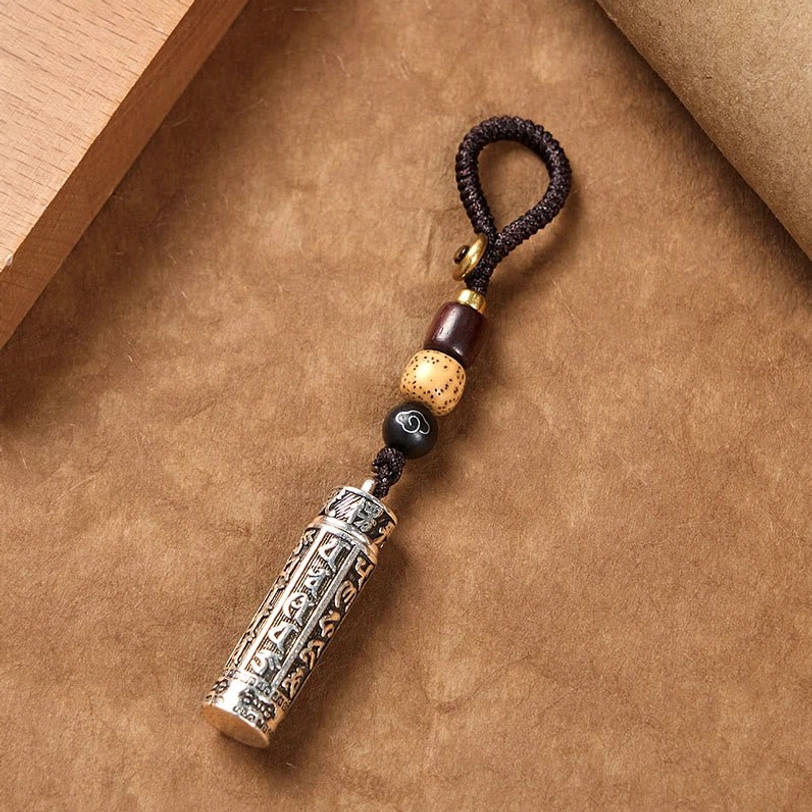 Tibetan Om Mani Padme Hum copper keychain flat lay, hand-engraved mantra pendant with braided lanyard and bodhi seed beads