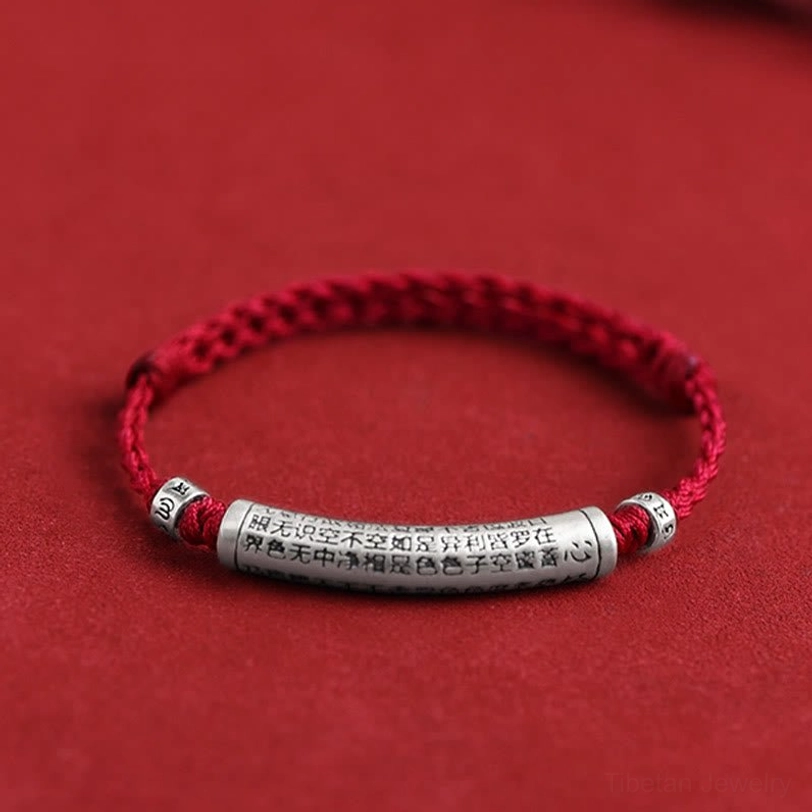 Handmade 999 sterling silver Om Mani Padme Hum bracelet with dark red braided rope and engraved Heart Sutra pendant, flat lay overhead view